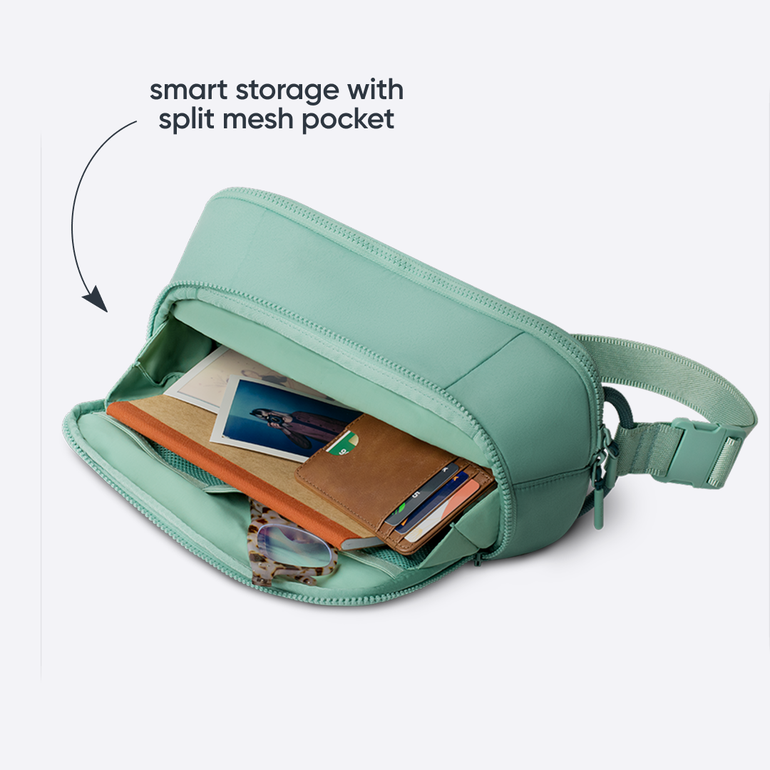 Owala All-Day Crossbody in Sea Glass, mint green body unzipped to show internal split mesh pocket holding cards, a wallet, and a phone, with text reading "smart storage with split mesh pocket"